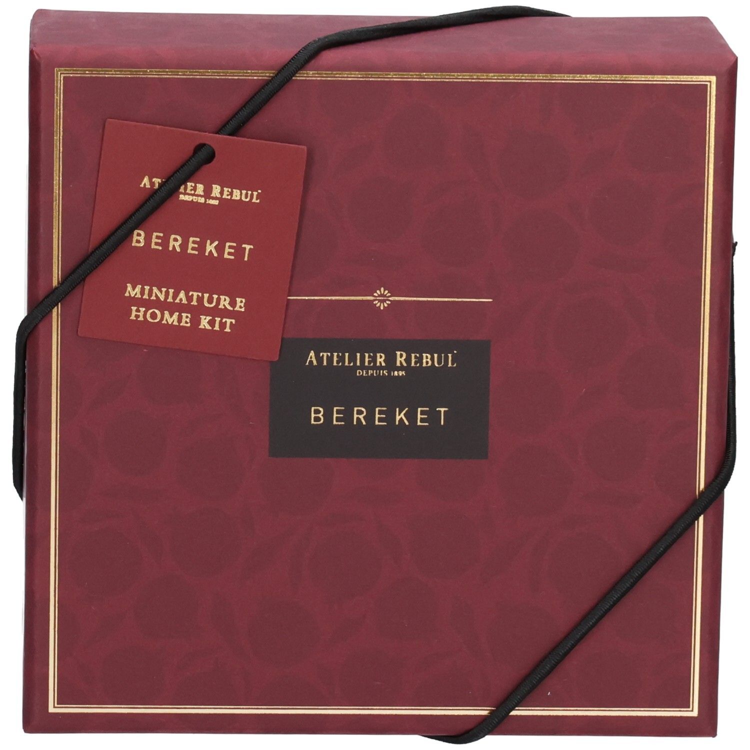 Coffret cadeau rouge avec bord doré et cordon noir. Étiquette avec nom du produit et logo.
