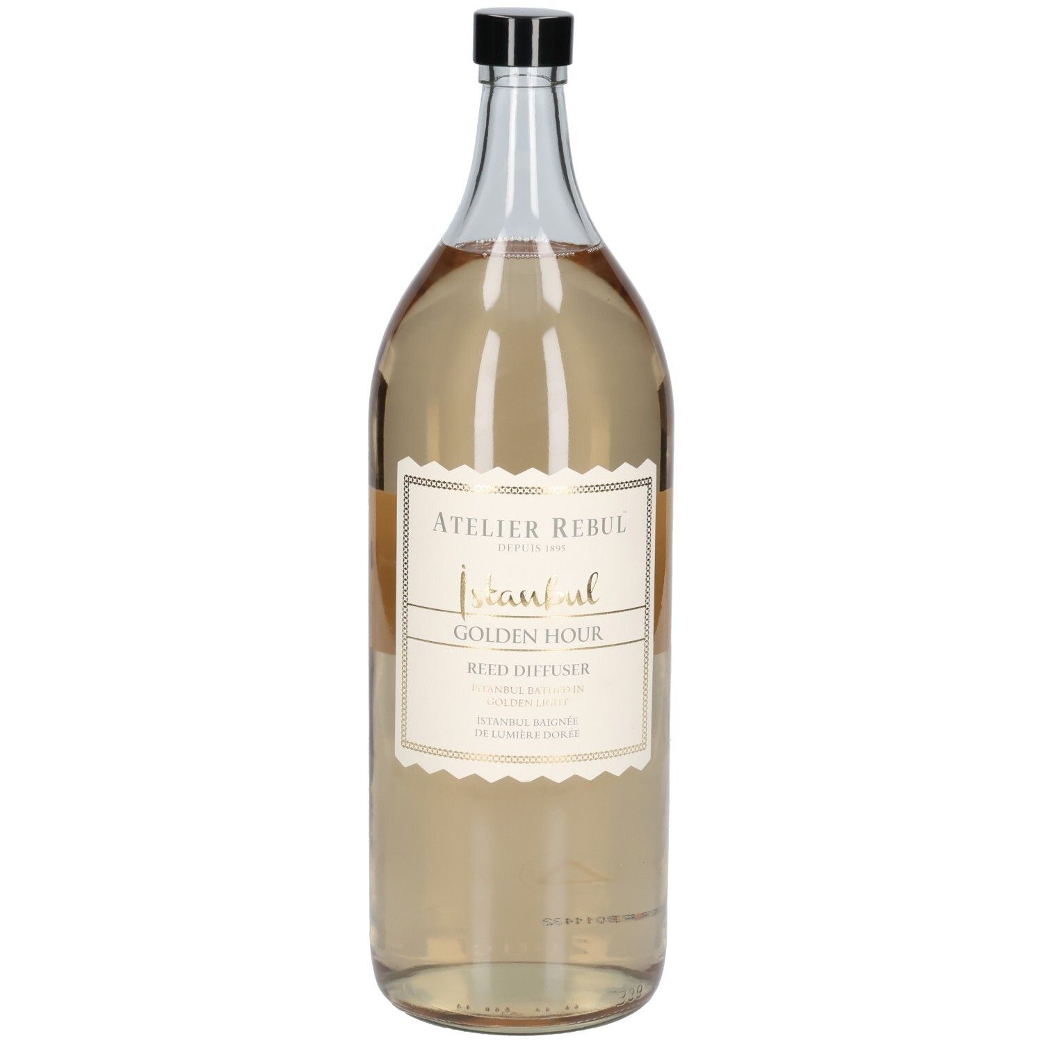 Grande bouteille en verre transparent avec bouchon noir. Étiquette avec texte doré : Atelier Rebul Istanbul Golden Hour Reed Diffuser.
