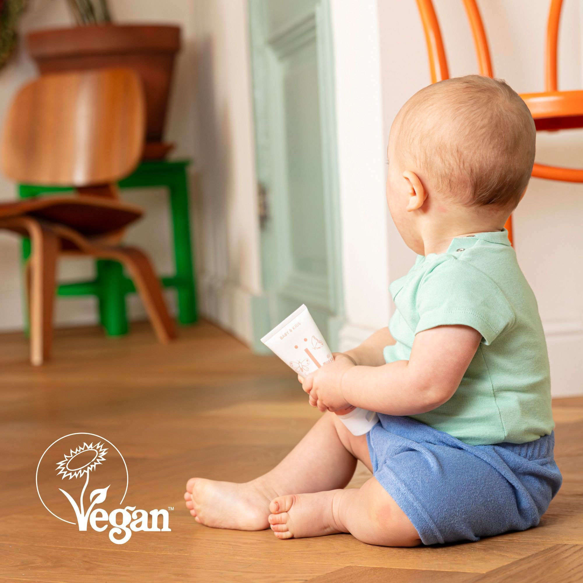 Bébé assis par terre tenant un tube de crème Naïf, avec label Vegan.
