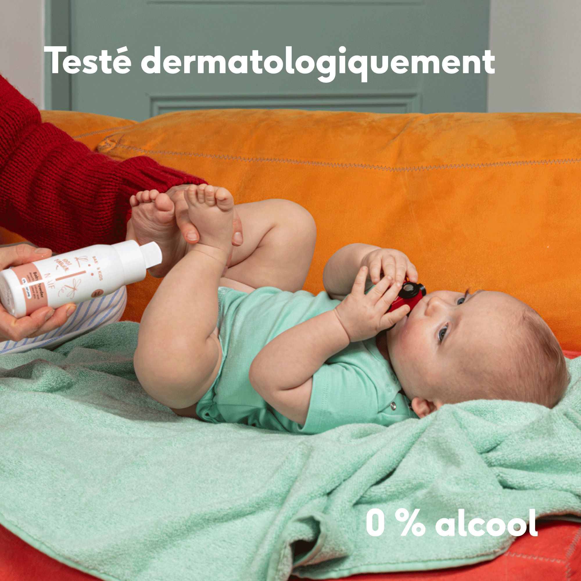 Une main tenant un flacon de Naïf Baby Powder près d'un bébé. Texte : '0% alcool'.