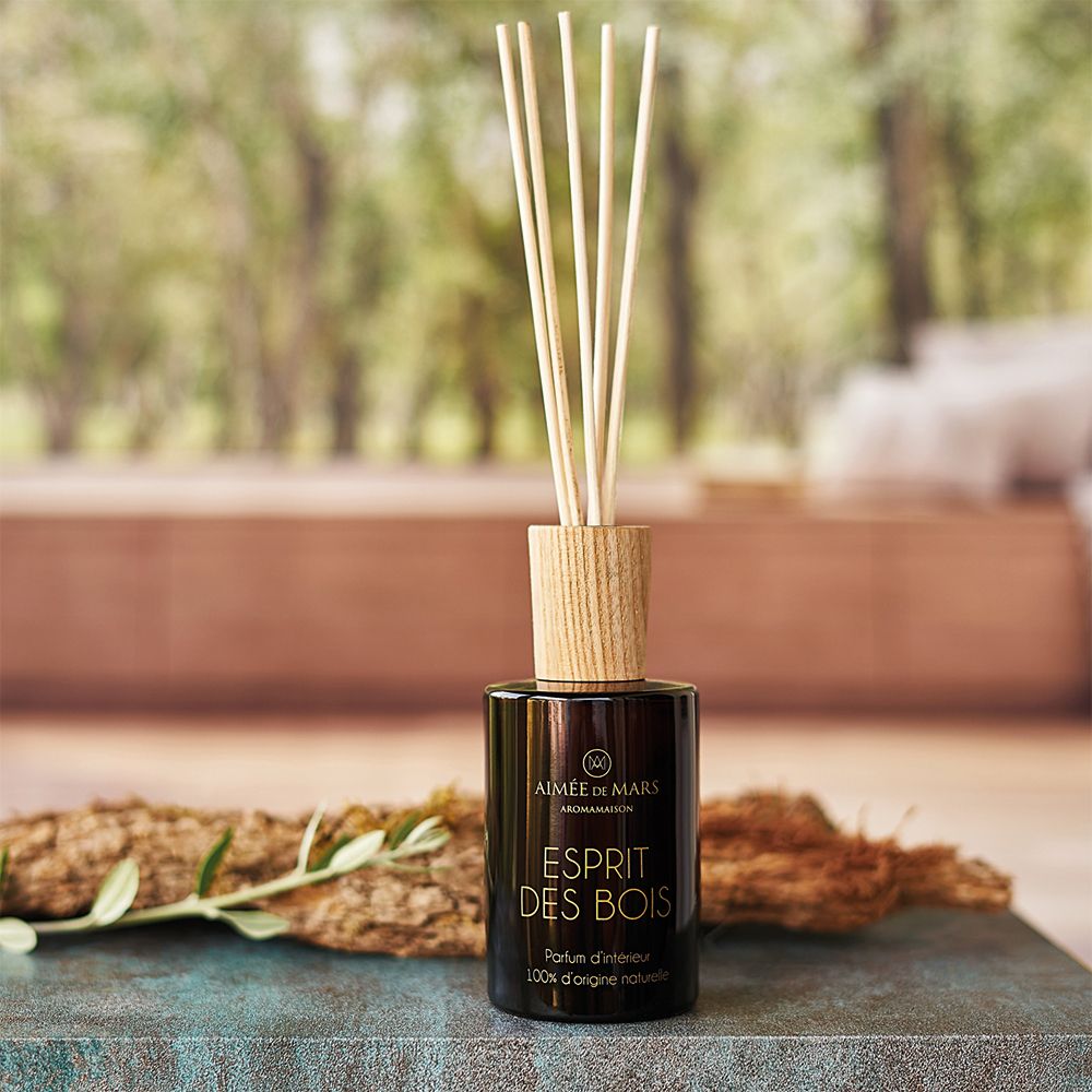 Flacon en verre brun avec bouchon en bois et bâtonnets. Nom du produit: Esprit des Bois. Fond: nature floue.