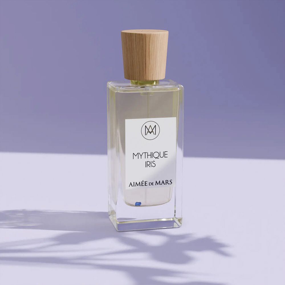 Flacon de parfum avec bouchon en bois. Inscription : Mythique Iris, Aimée de Mars. Flacon rectangulaire en verre sur fond violet.