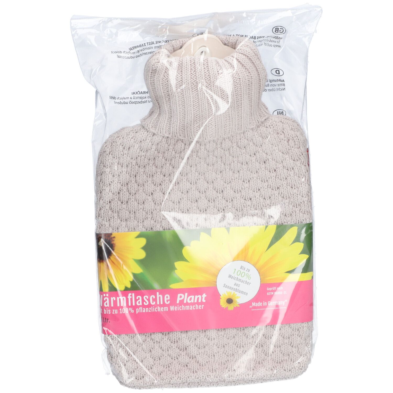 Bouillotte dans un emballage transparent. Housse en tricot beige, bande verte avec logo et tournesol. Texte : Bouillotte Plant.