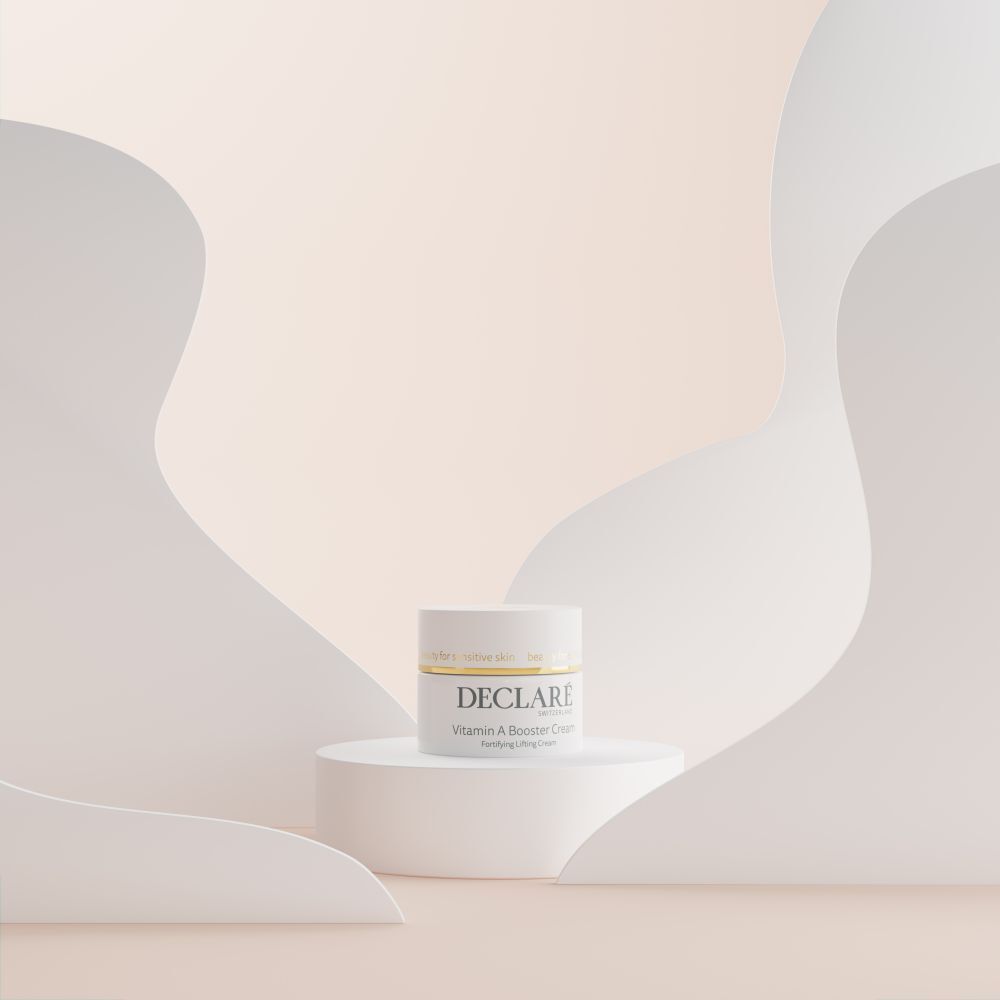 Pot blanc sur socle. Fond avec formes blanches incurvées. DECLARÉ Vitamin A Booster Cream.