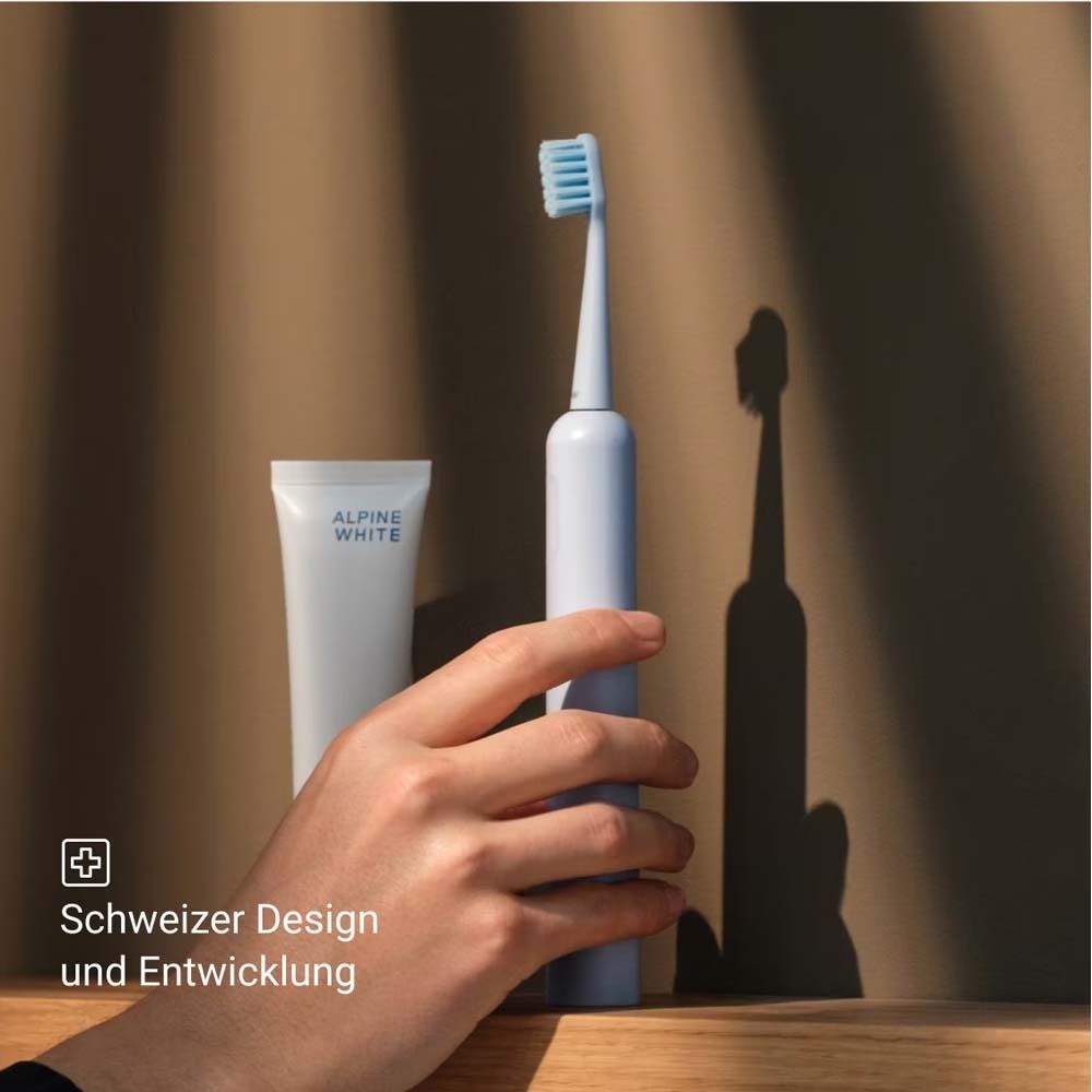 Une brosse à dents électrique bleue, du dentifrice et une main. Design et développement suisses.