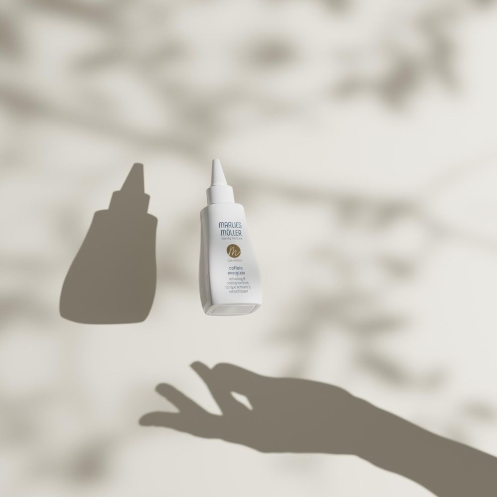 Flacon blanc avec applicateur pointu, en suspension. Ombres d'une main et de feuilles.