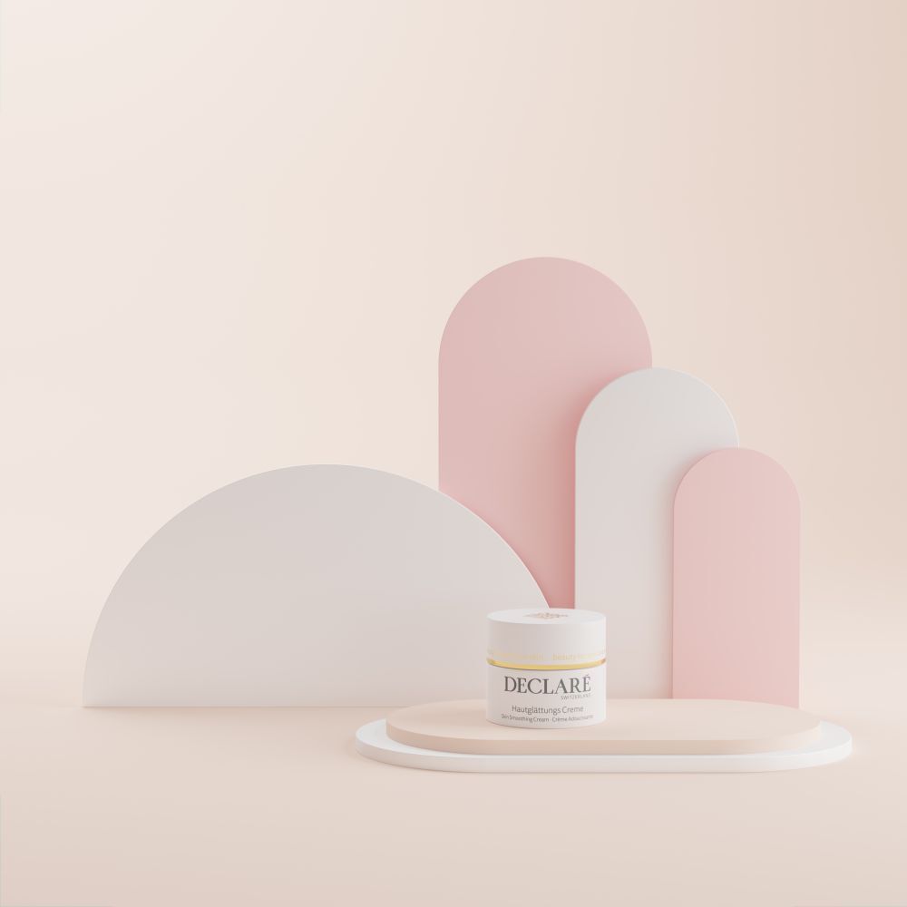 Pot de crème sur une plateforme ovale. Fond : formes géométriques blanches et roses. Inscription : DECLARÉ, Hautglättungs Creme.