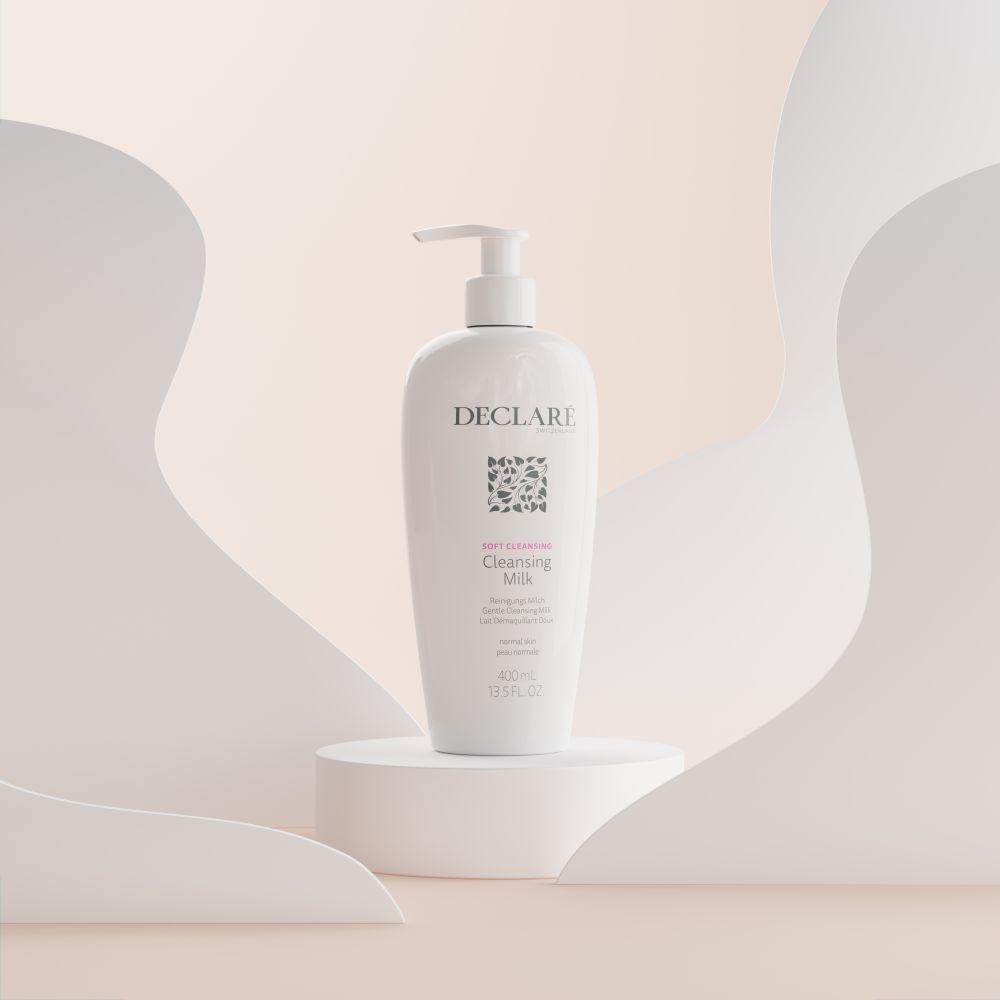Flacon blanc DECLARÉ Cleansing Milk sur socle. Fond avec formes blanches.