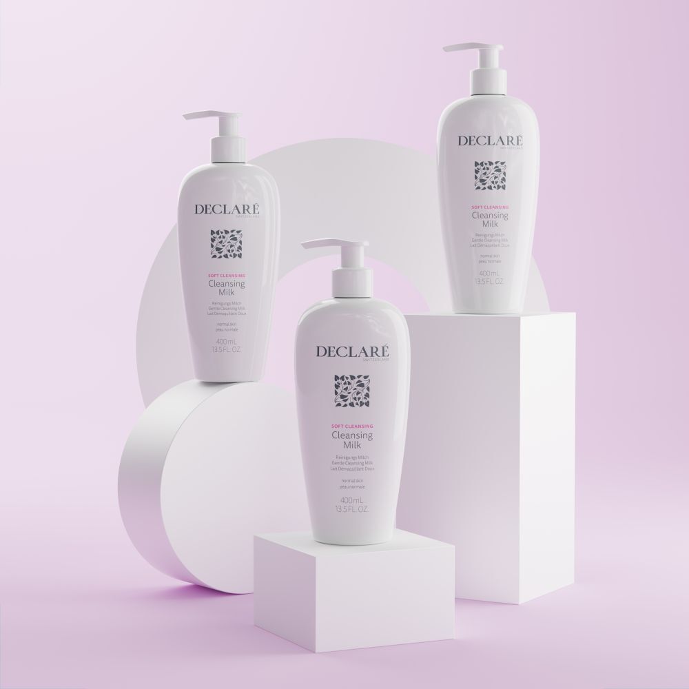 Trois flacons blancs DECLARÉ Cleansing Milk sur socles. Arrière-plans roses et blancs.