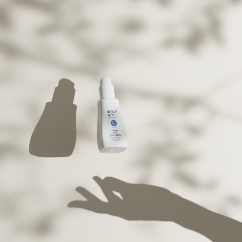 Spray blanc Marlies Möller, ombre d'une main. Texte: Volume Boost Styling Spray.