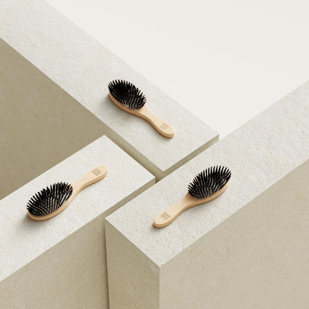 Trois petites brosses à cheveux ovales sur blocs blancs. Manche en bois, soies noires.