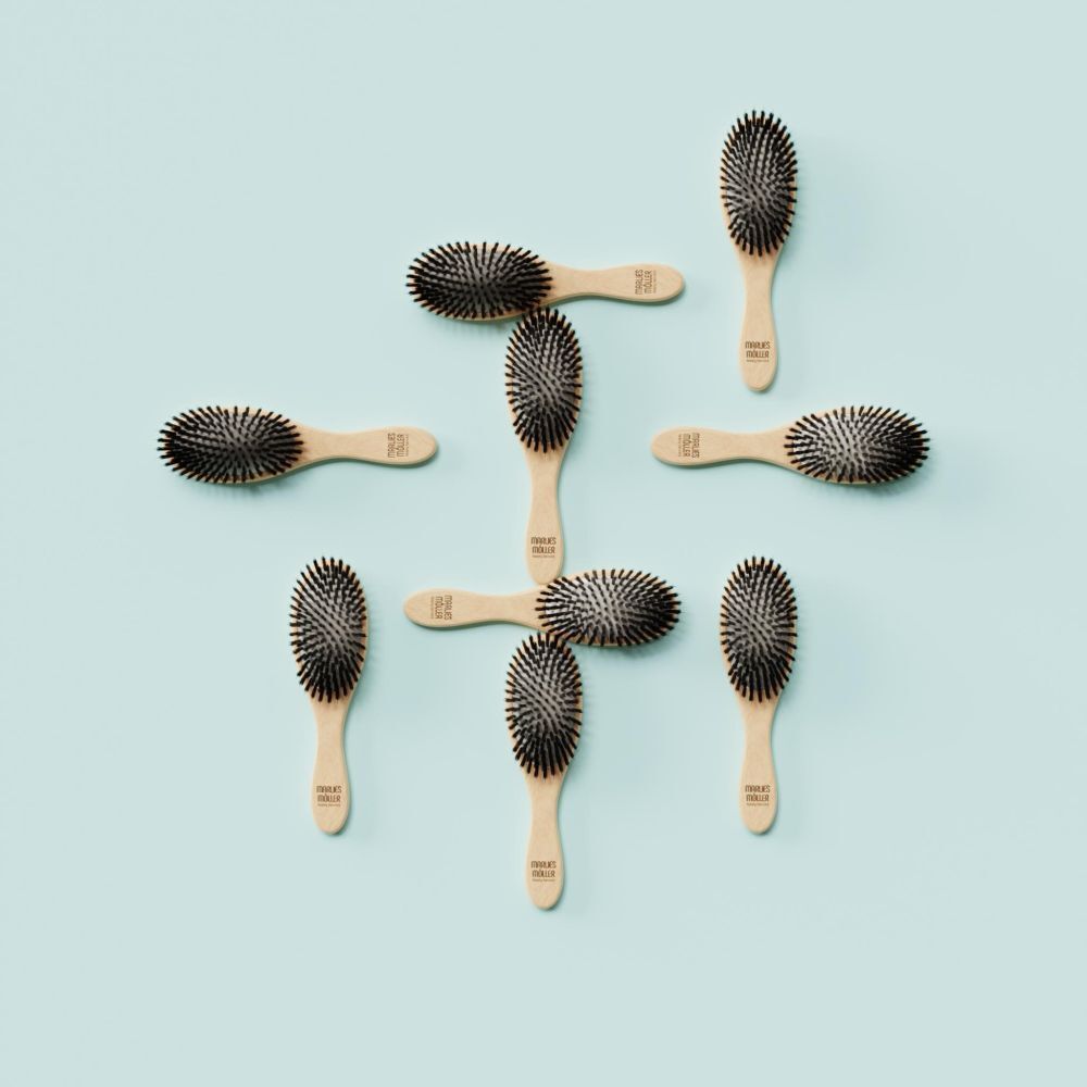 Plusieurs petites brosses à cheveux ovales sur fond turquoise. Manche en bois, soies noires.