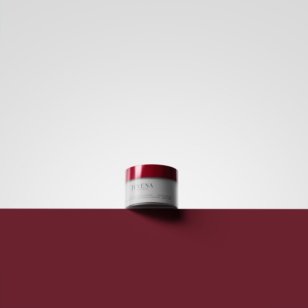 Pot de crème à couvercle rouge sur fond blanc et bordeaux. Logo Juvena visible.
