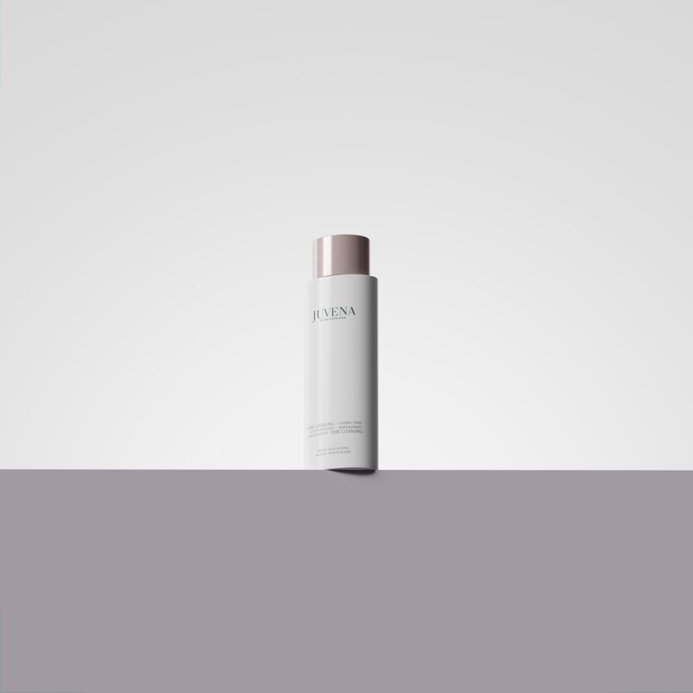 Flacon blanc avec bouchon rose. Inscription : Juvena. Placé sur une surface violette.
