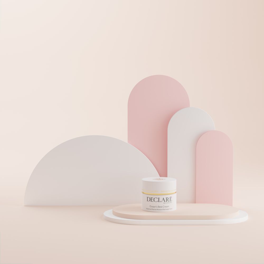 Pot blanc sur socle. DECLARÉ Ocean's Best Cream. Fond: formes roses et blanches.