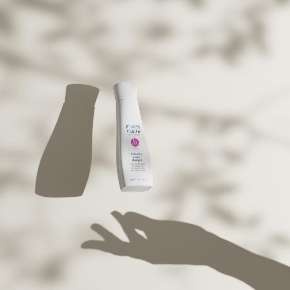 Flacon blanc de shampooing Marlies Möller. Ombres de feuilles et de main. Texte: Colour Brilliance Shampoo.