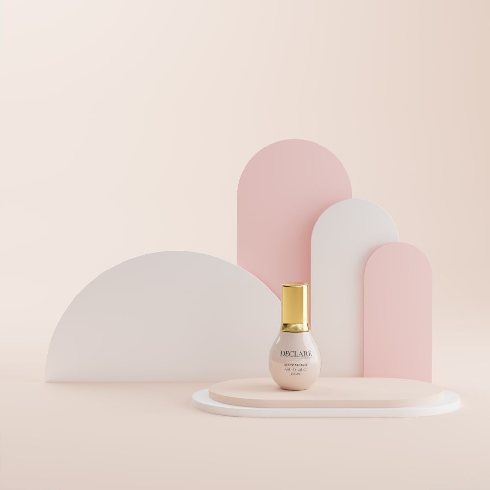 Flacon de sérum rose avec bouchon doré sur un socle. Formes décoratives en arrière-plan.