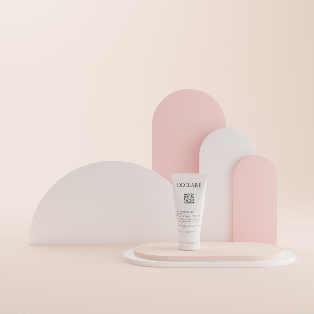 Tube DECLARÉ CC Cream SPF 30 sur un piédestal. Fond avec formes roses et blanches.