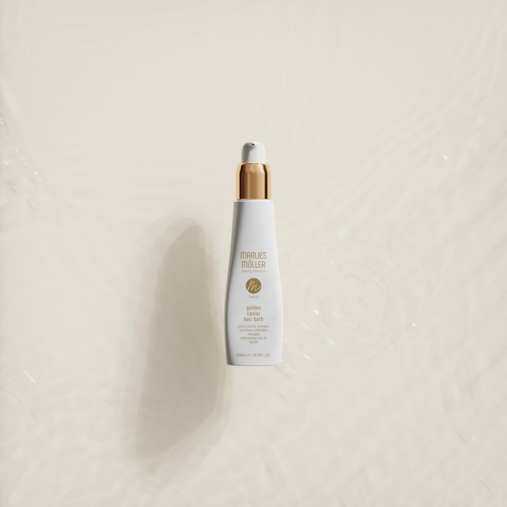 Flacon blanc avec bouchon doré. Inscription: Marlies Möller, Luxury Golden Caviar Hair Bath. Sur l'eau.