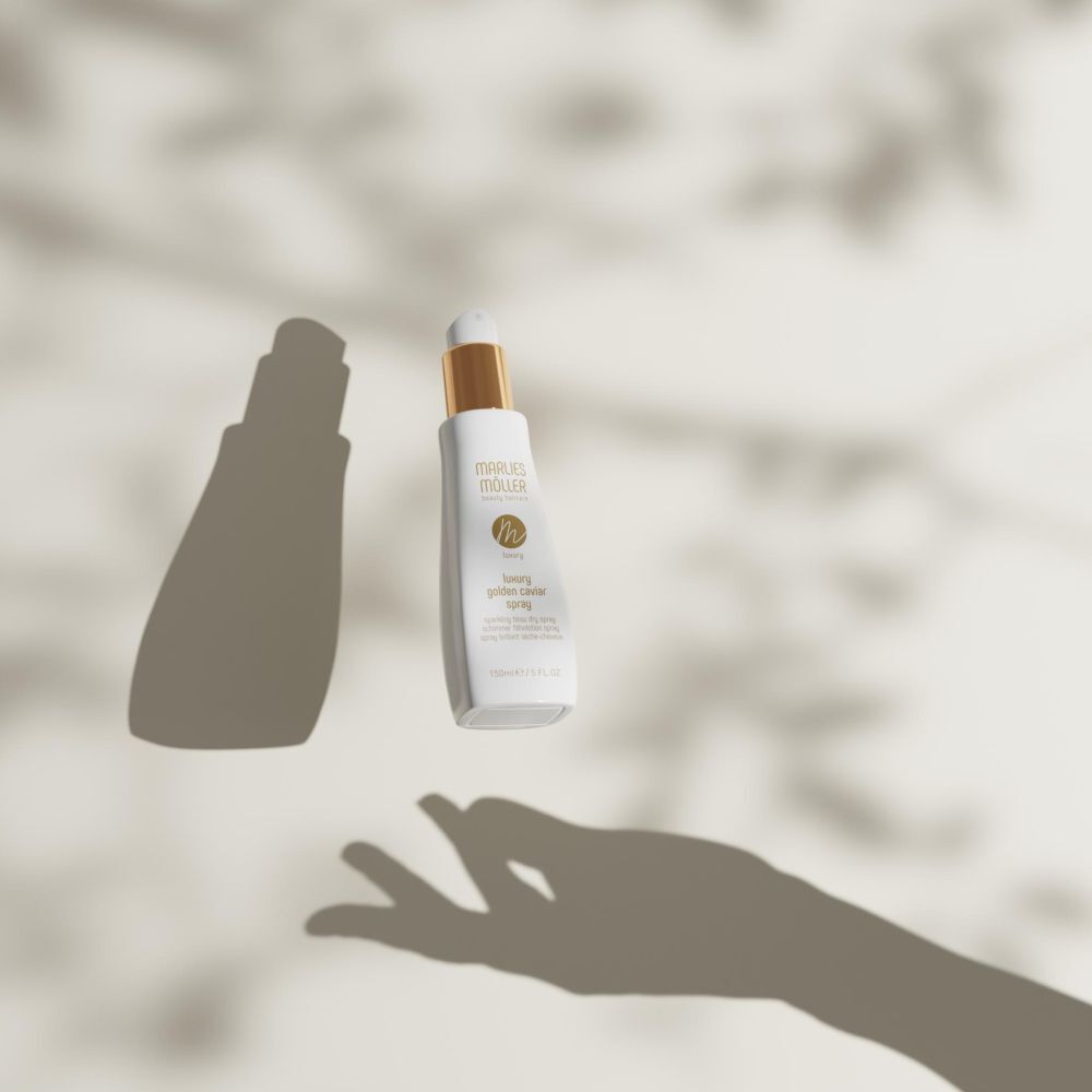 Spray avec bouchon doré flottant. Ombres d'une main et de feuilles. Inscription: Marlies Möller, Luxury Golden Caviar Spray.