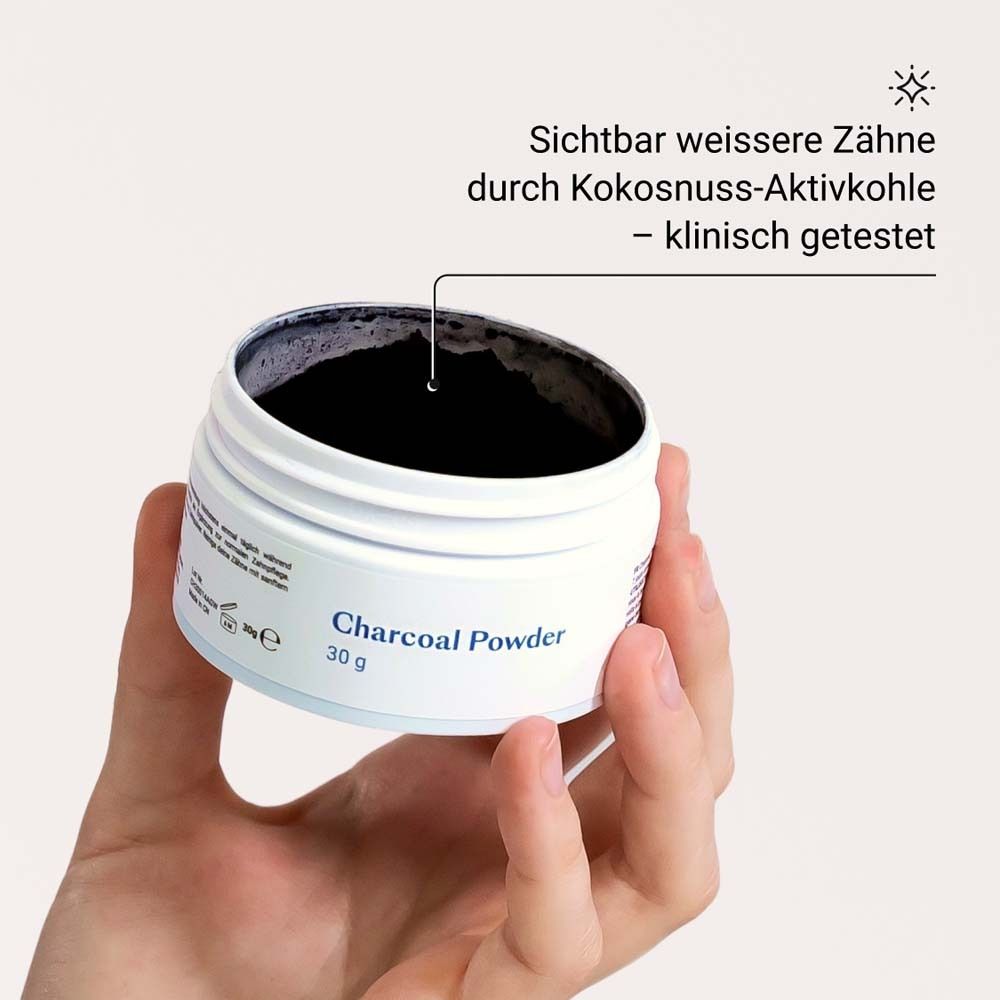Main tenant un pot de poudre noire. Texte: Charcoal Powder, 30 g.