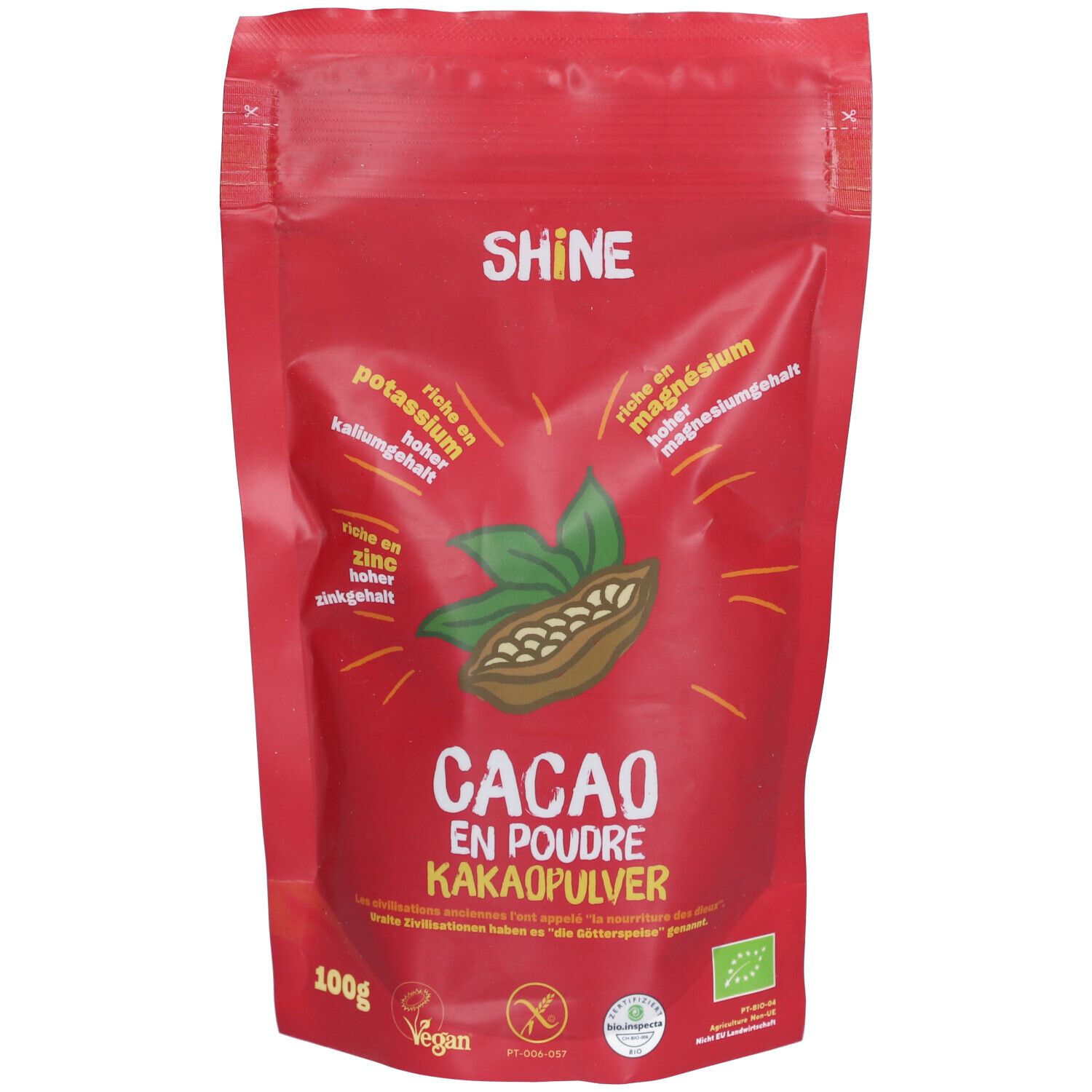 Sachet rouge de poudre de cacao SHINE. Inscription "CACAO EN POUDRE KAKAOPULVER". Contient des feuilles et une fève de cacao.