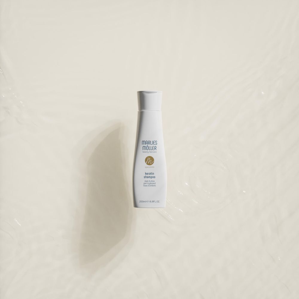 Bouteille de shampooing Marlies Möller Kératine sur fond clair avec des ondulations d'eau.