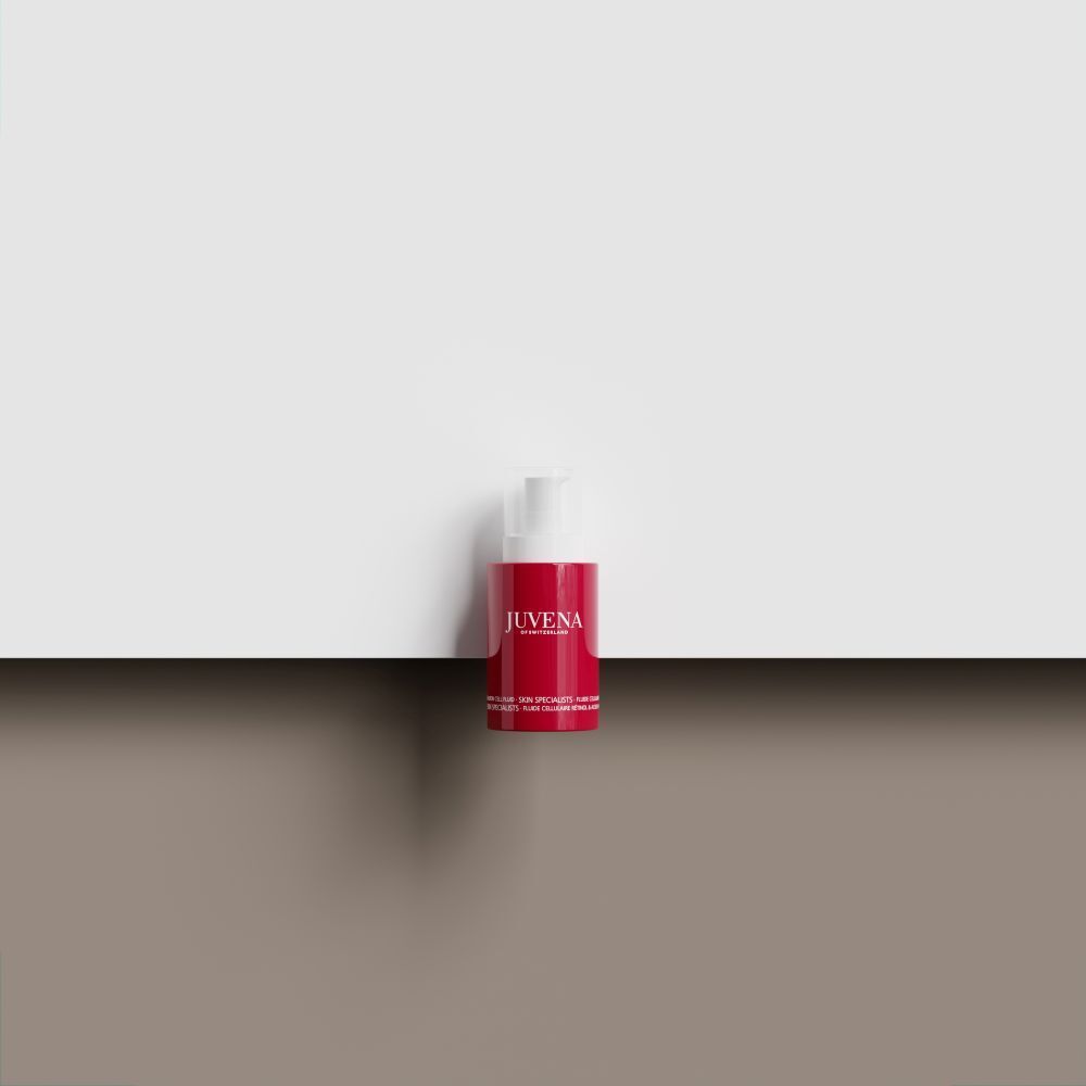 Flacon rouge avec bouchon blanc. Inscription: JUVENA. Posé sur une surface marron devant un fond blanc.