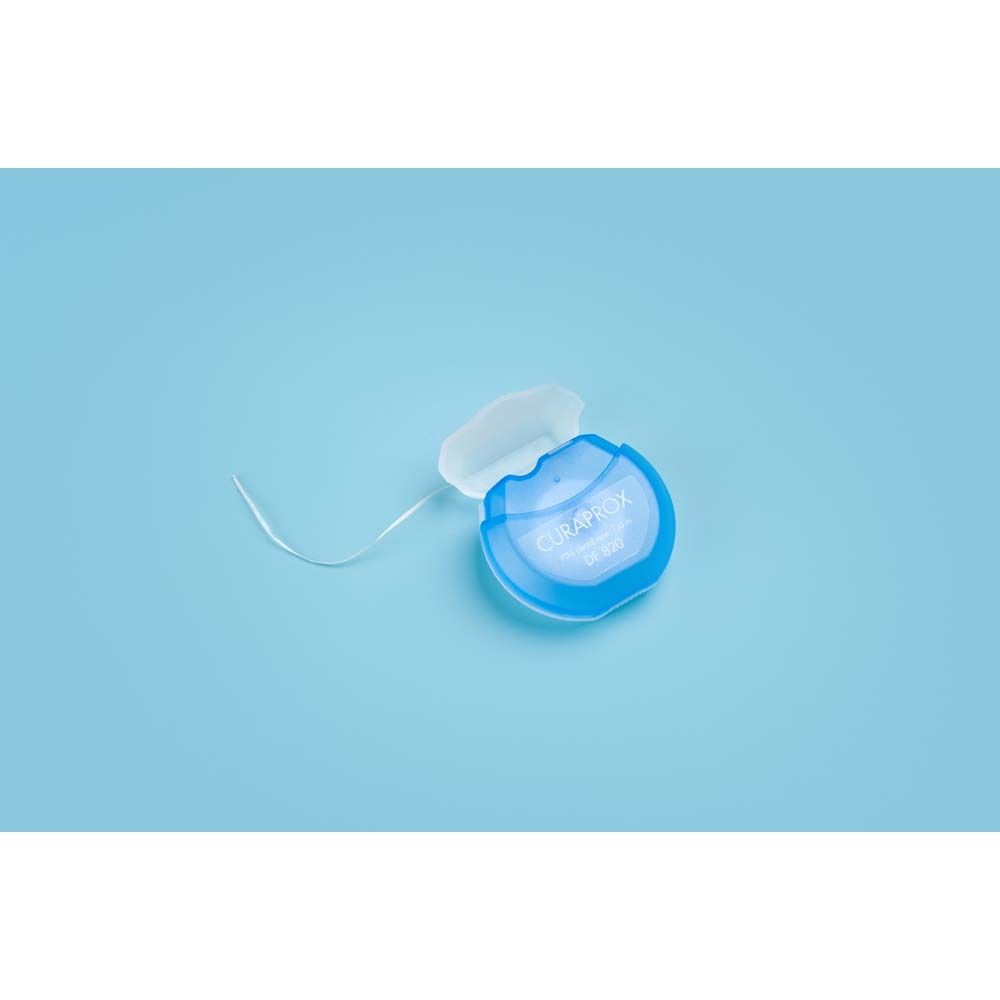 Distributeur de fil dentaire bleu avec capuchon blanc. Fil visible. Sur fond bleu.