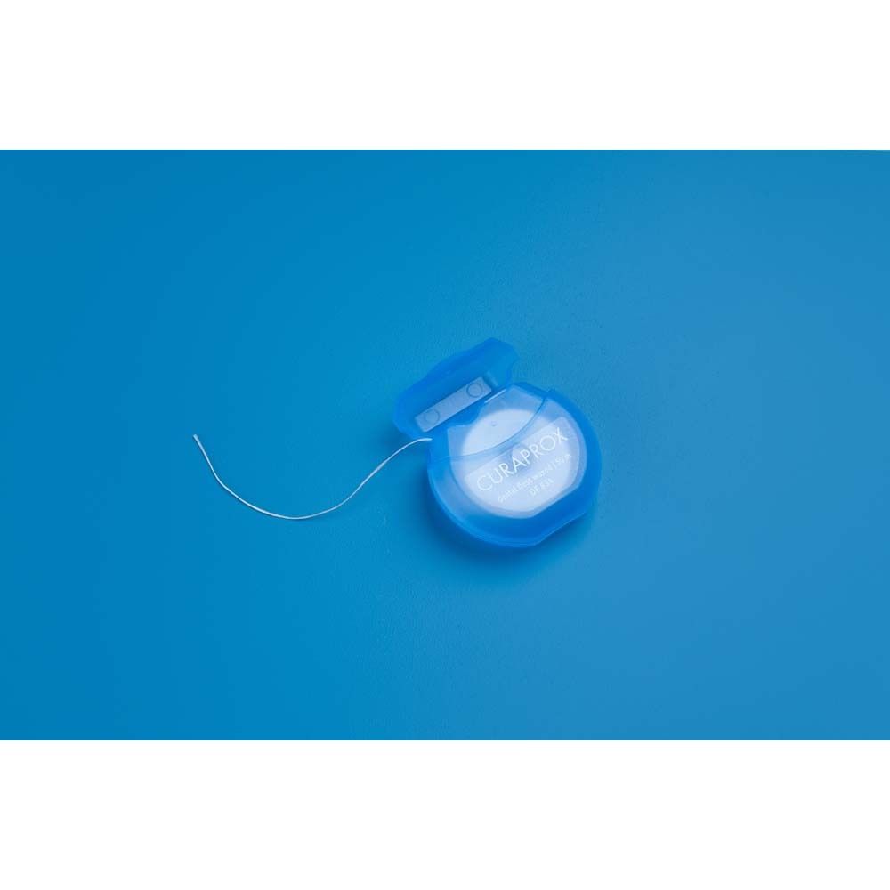 Bobine de fil dentaire bleu avec fil sorti. Sur fond bleu.