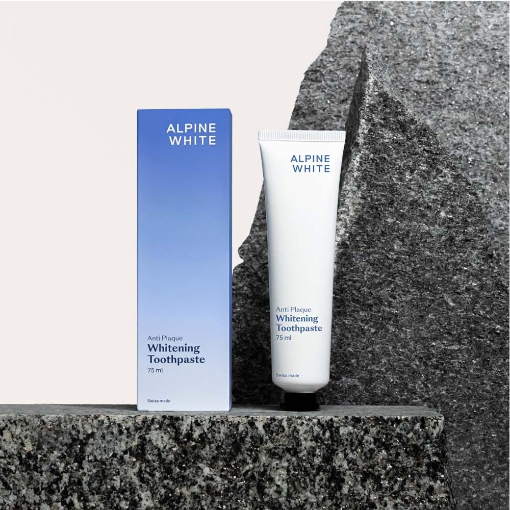Dentifrice et boîte sur pierre. Boîte bleue et tube blanc. Texte: ALPINE WHITE, Anti-Plaque, Whitening Toothpaste.