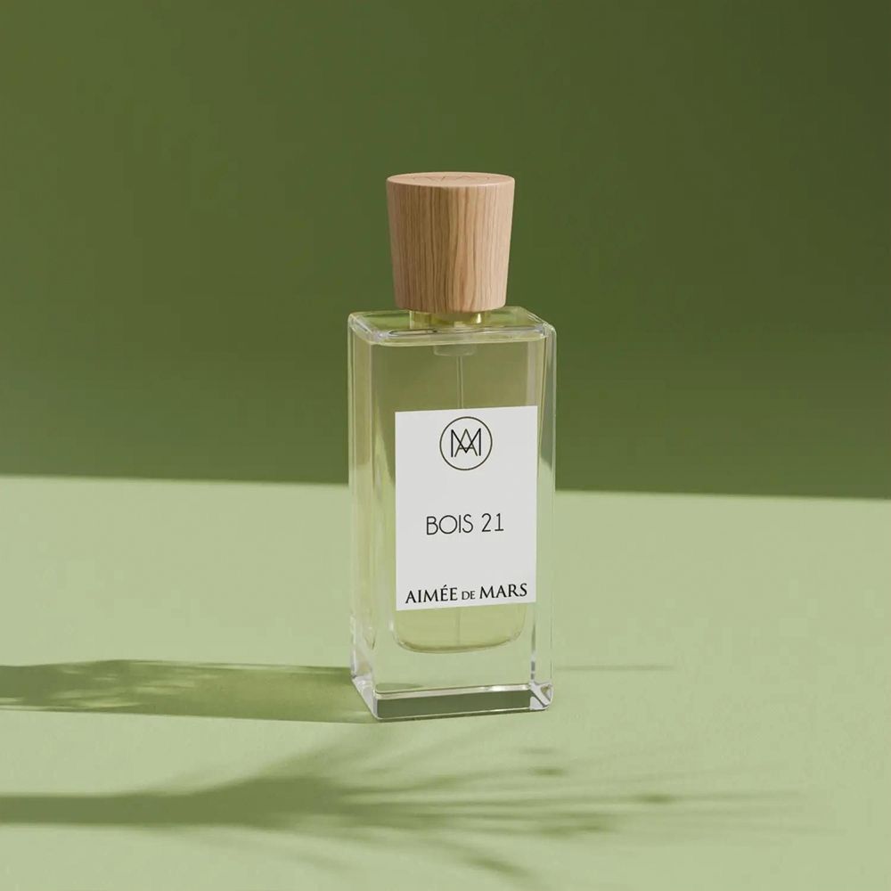Flacon en verre avec bouchon en bois sur fond vert. Étiquette avec logo, texte « Bois 21 » et « Aimée de Mars ». Liquide visible.