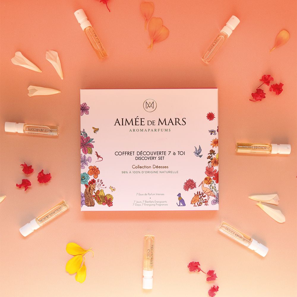 Échantillons de parfum et pétales sur fond rose. Coffret cadeau au centre. Plusieurs petits flacons en verre.