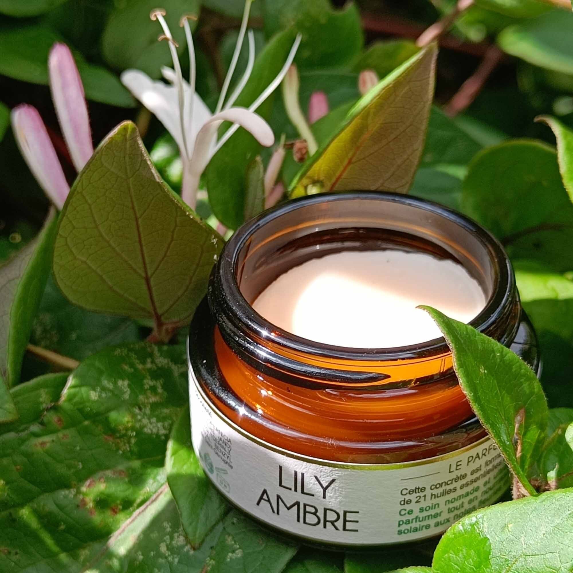 Pot en verre brun avec contenu crème, entouré de feuilles et fleurs vertes. Inscription "LILY AMBRE".