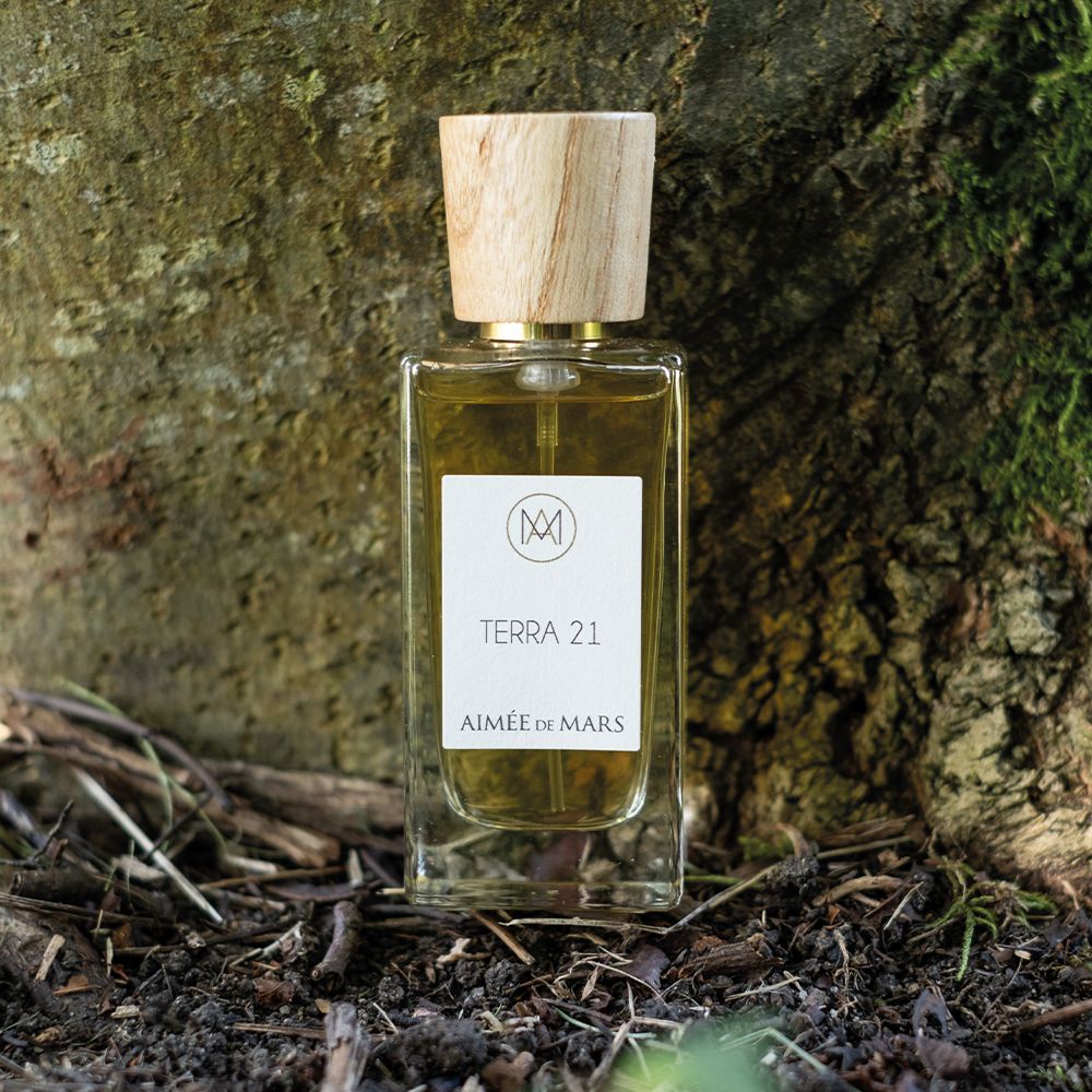Flacon en verre avec bouchon en bois devant un tronc d'arbre. Étiquette avec texte: Terra 21, Aimée de Mars.