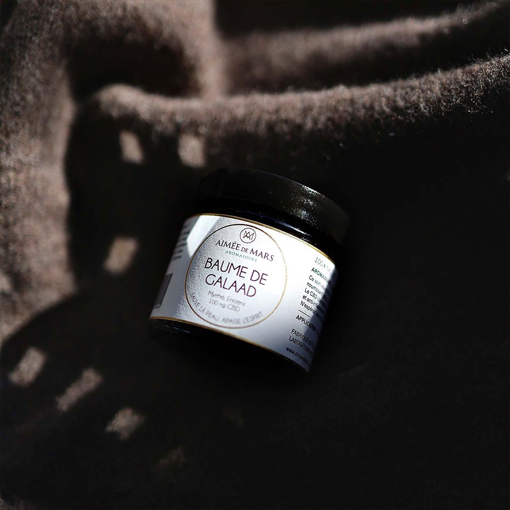 Pot noir sur fond marron. Étiquette : AIMÉE DE MARS, Baume de Galaad, Myrrhe, Encens, 100 mg CBD.
