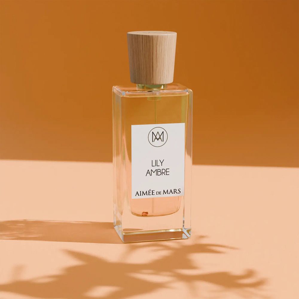 Flacon de parfum avec bouchon en bois. Inscription : LILY AMBRE, AIMÉE DE MARS. Flacon rectangulaire en verre, liquide doré.
