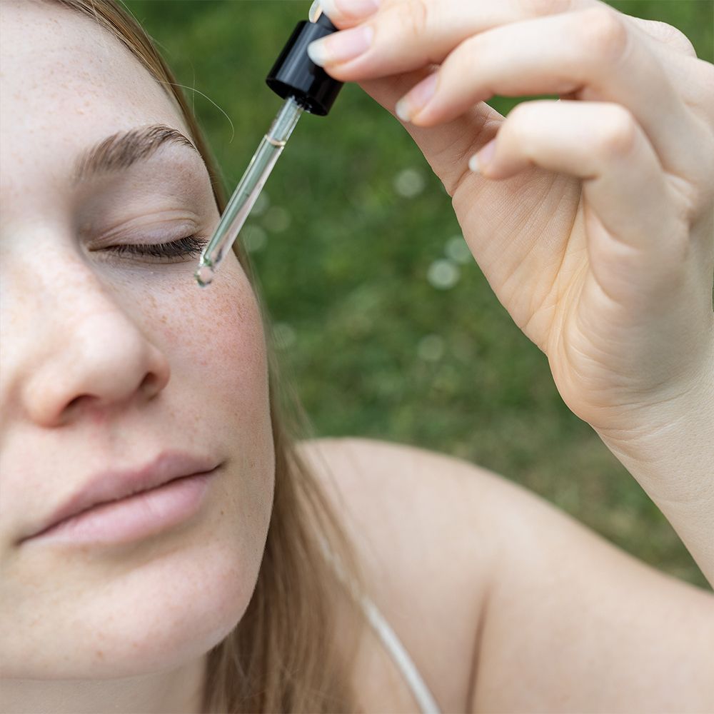 Femme aux yeux fermés. Compte-gouttes dépose du liquide sur la peau. Fond vert.