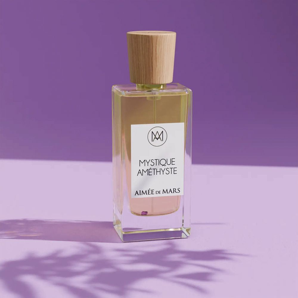 Flacon carré avec bouchon en bois, liquide ambré, étiquette blanche: Mystique Améthyste, Aimée de Mars. Sur fond violet.
