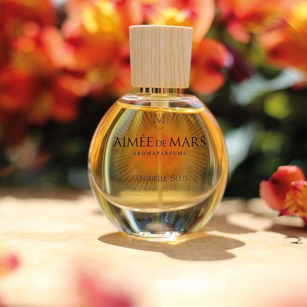 Flacon rond en verre avec bouchon en bois. Inscription : Aimée de Mars Aromaparfums, Sensuelle Sulis. Liquide doré.