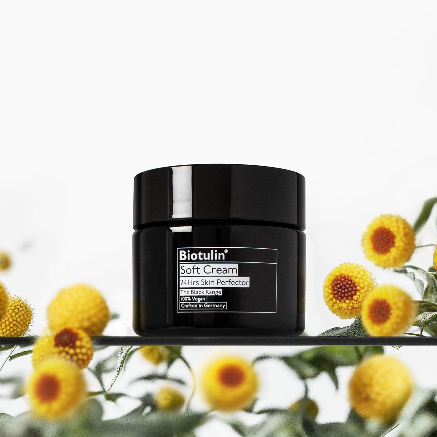 Pot noir avec Biotulin Soft Cream sur une étagère avec des fleurs.