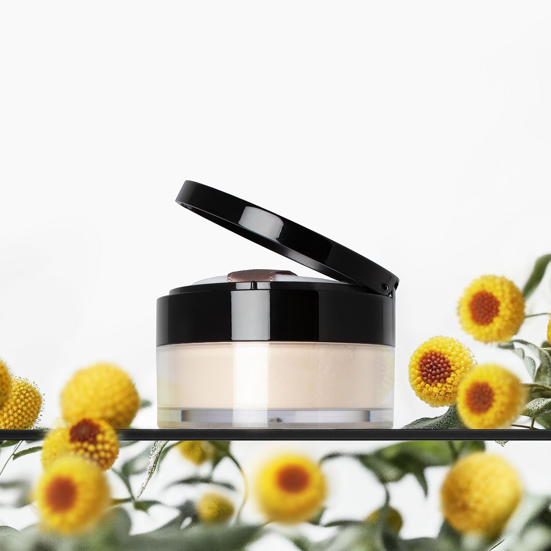 Boîte de poudre avec couvercle noir. Fleurs jaunes et feuilles vertes en arrière-plan.