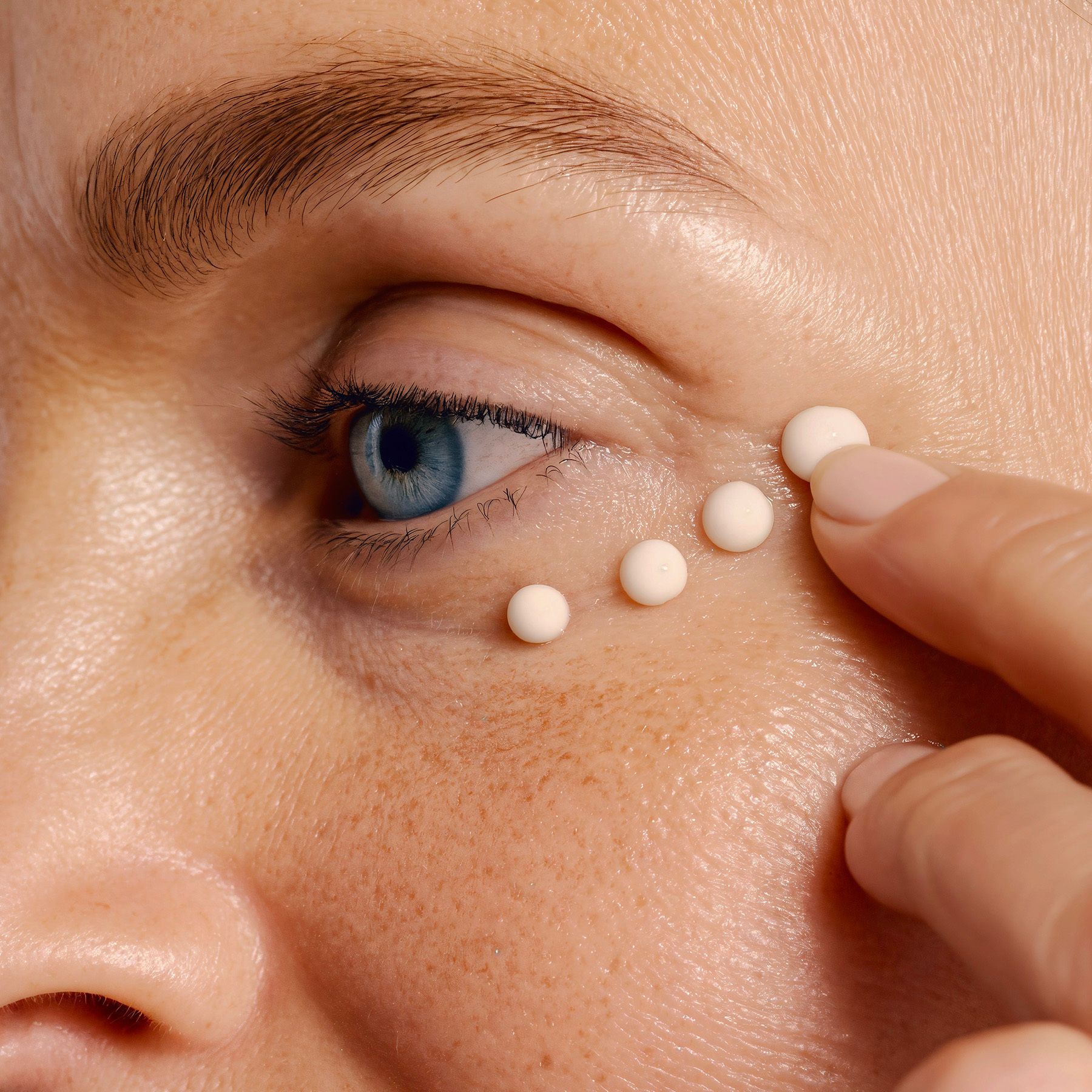 Gros plan sur un œil avec des points de crème. Aucun nom de produit visible.