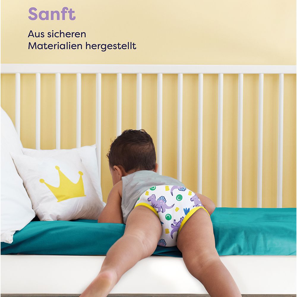 Enfant avec culotte d'apprentissage sur lit. Texte : Doux. Fabriqué avec des matériaux sûrs. Oreiller couronne jaune.
