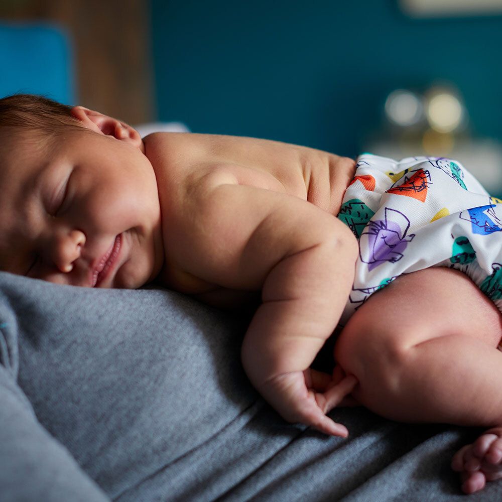 Bébé sur les bras, portant une couche à motifs colorés.