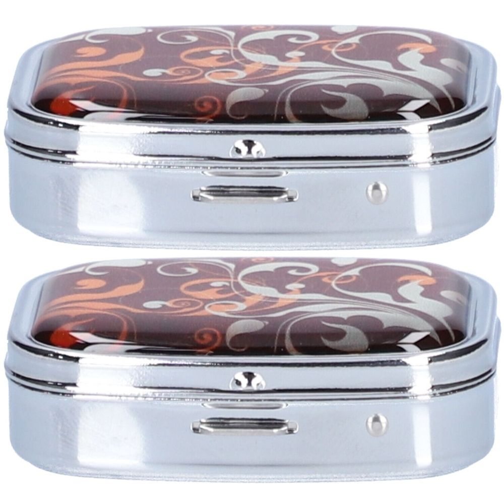 Deux piluliers rectangulaires avec motifs floraux sur le couvercle. Cadre métallique, deux compartiments. Couleurs assorties.