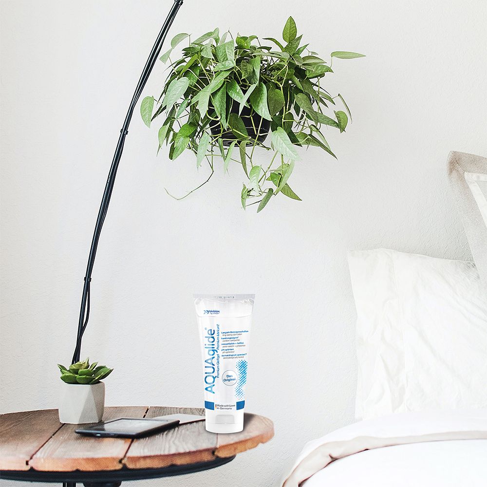 Tube AQUAGLIDE sur une table de chevet près d'une plante et d'une lampe.