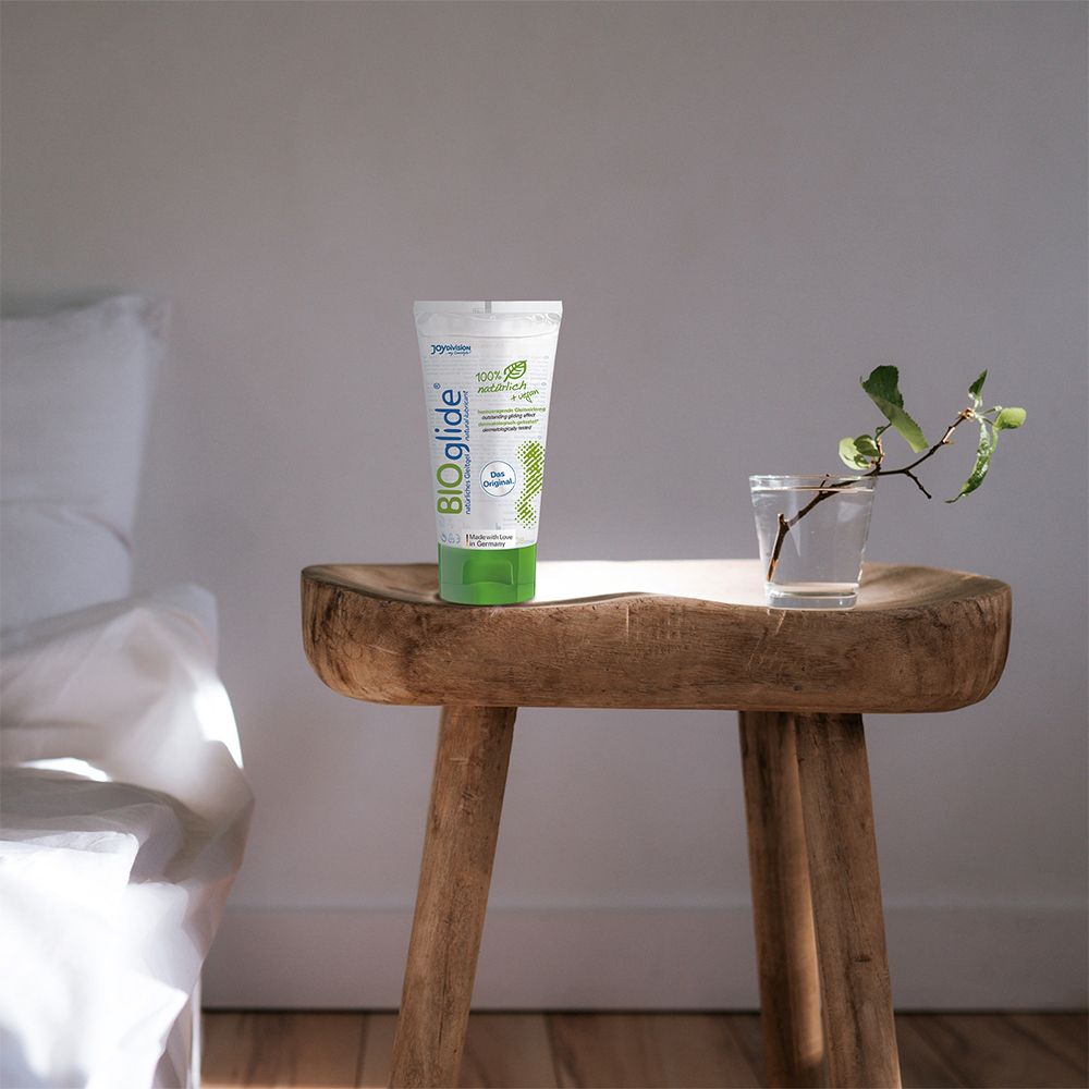 Tube BIOglide sur un tabouret en bois près d'un verre d'eau et d'une plante.
