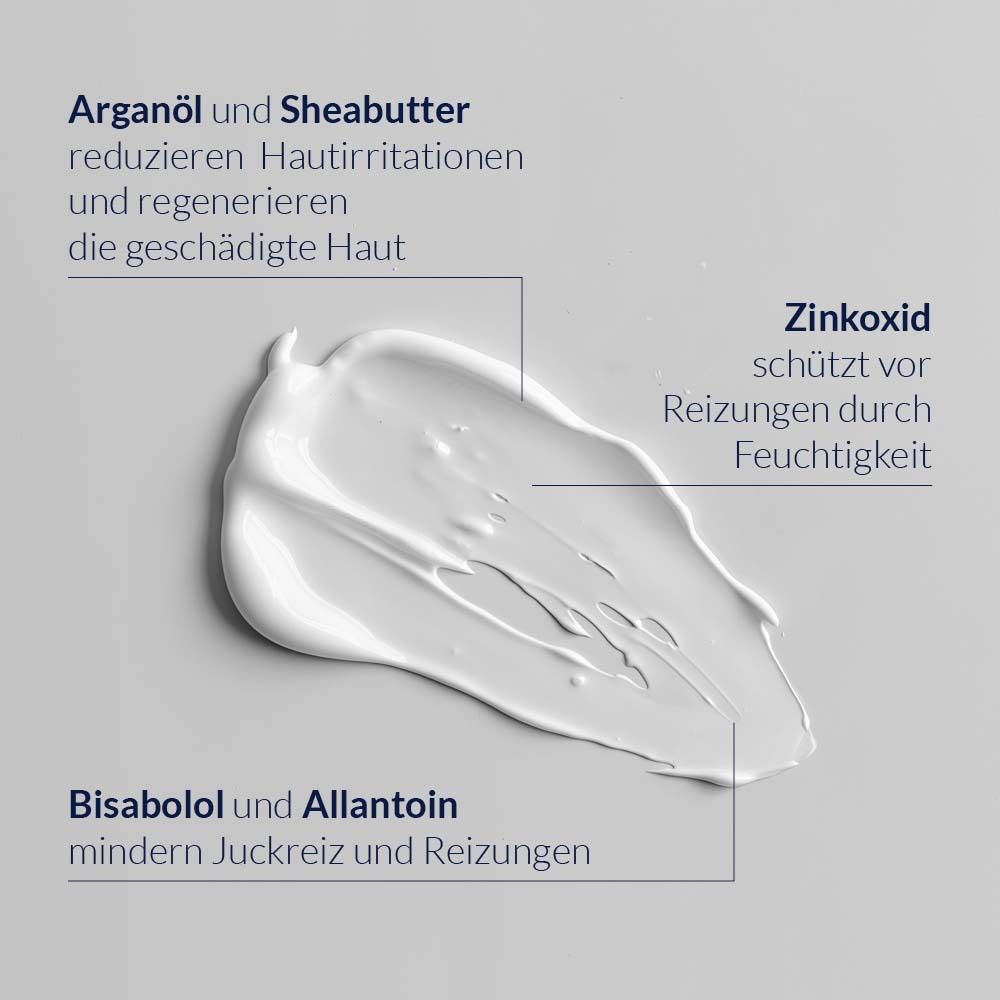 Gros plan d'une crème. Inscriptions : Huile d'argan et beurre de karité, oxyde de zinc, bisabolol et allantoïne. Fond gris.