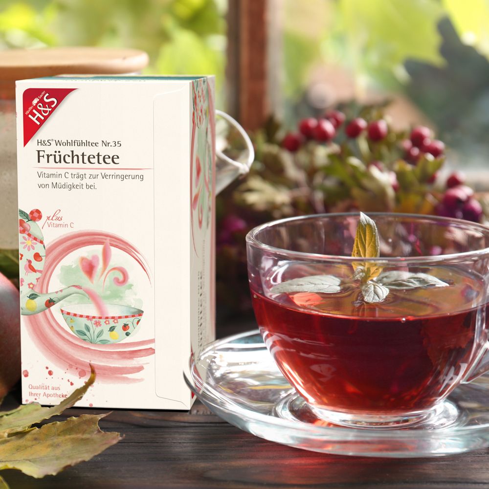 Boîte de H&S Thé aux fruits avec Vitamine C N°35 à côté d'une tasse de thé. Vue sur table en bois.